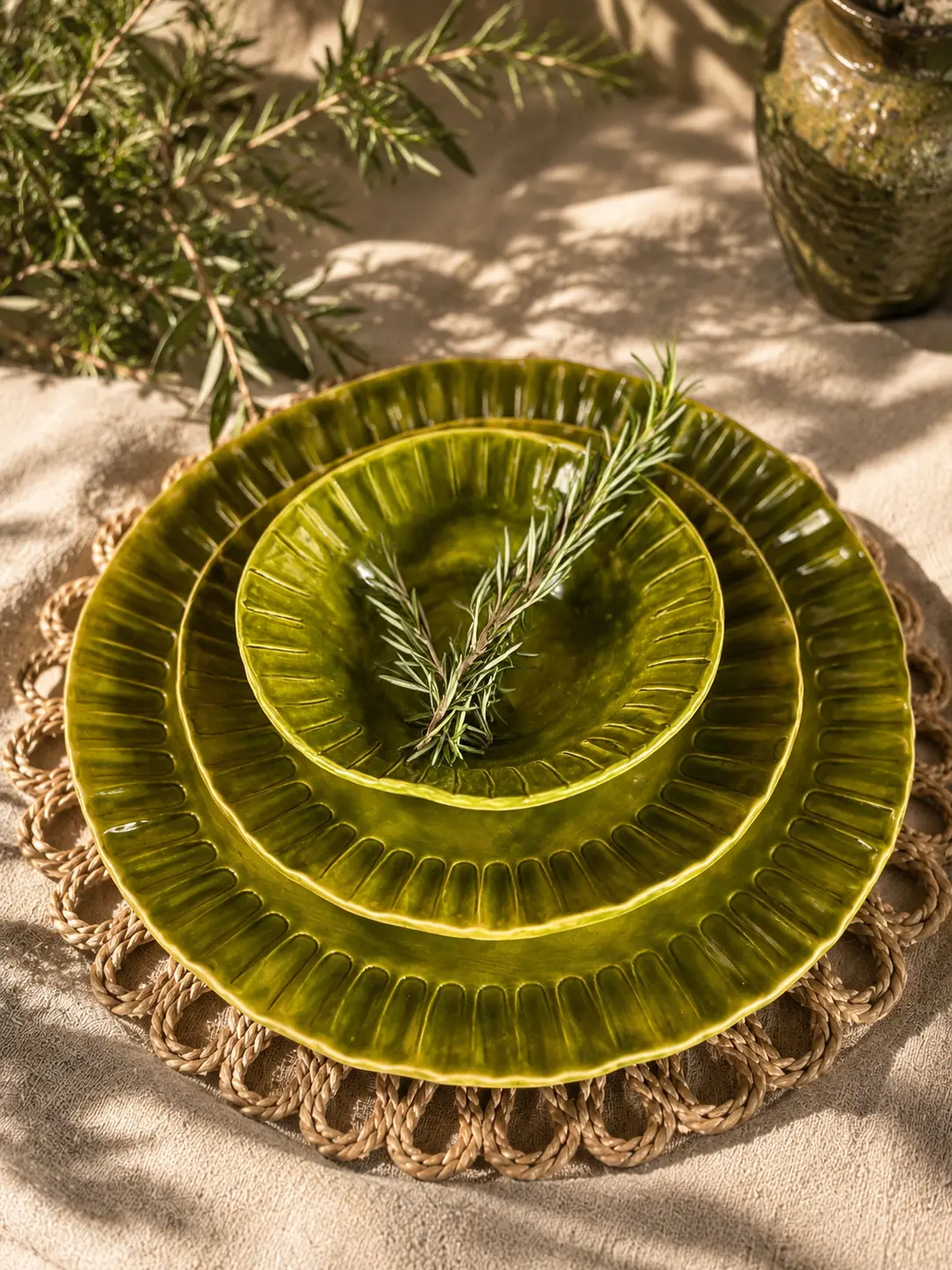 Sunlit olive green handmade ceramic plates on woven placemat with rosemary